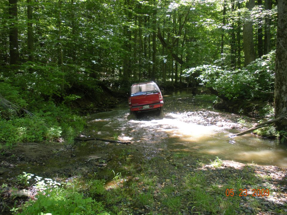 Red SUV driving through a stream, rear view. The vehicle appears to be from the mid-1990s