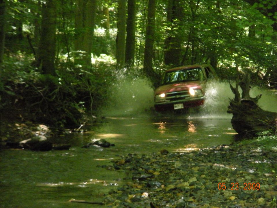 Red 1998 Chevrolet Blazer driving through stream, kicking up water