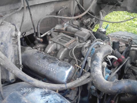 1986 Ford Bronco - A close-up view of a cluttered engine bay, showing various mechanical components and hoses.