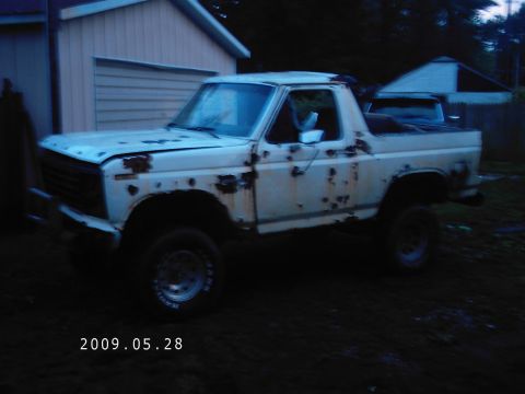 1986 Ford Bronco - This heavily rusted white SUV is parked outside a building, showing significant body damage.
