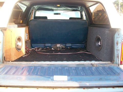 1982 Ford Bronco - The rear cargo area of a vehicle shows custom audio equipment, including two subwoofer boxes and amplifiers.