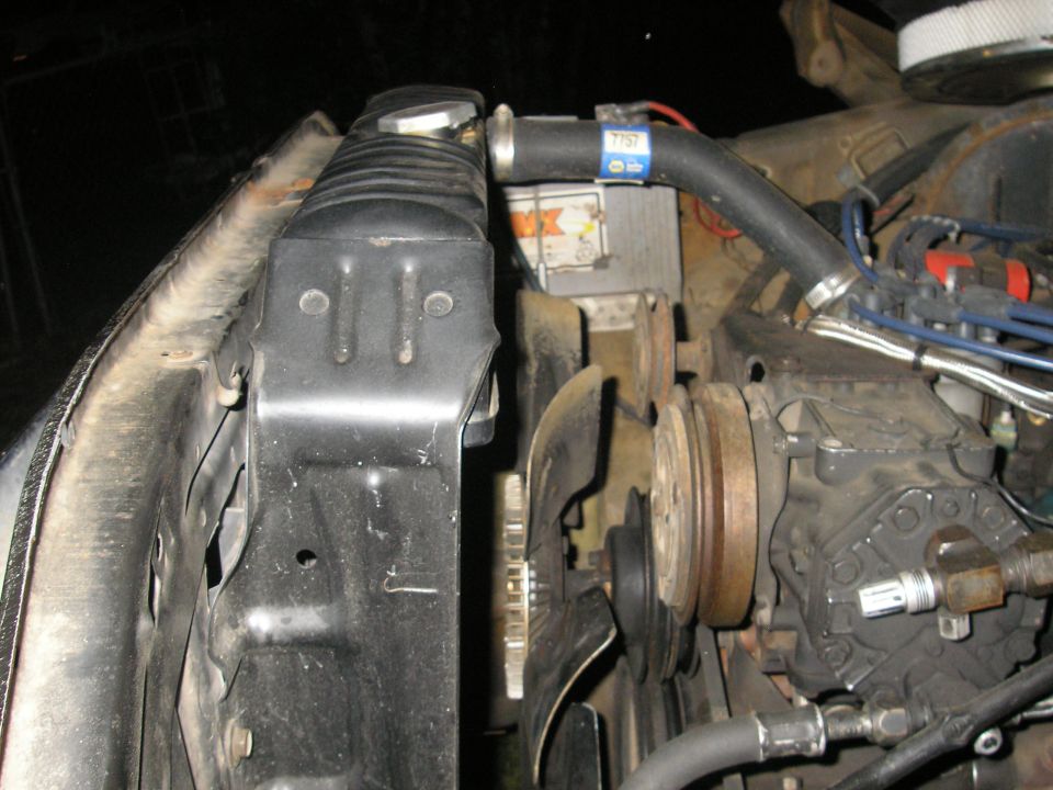 Engine bay of a Ford Bronco showing radiator, upper hose with NAPA clamp, fan and pulleys at night