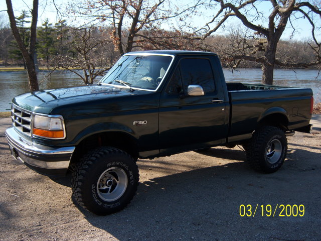 Dark green 1996 Ford F-150 pickup truck with lifted suspension and aftermarket wheels parked outdoors