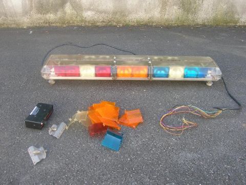 1991 Ford Crown Victoria - A police light bar and its disassembled parts are laid out on asphalt, including various colored lenses and wiring.