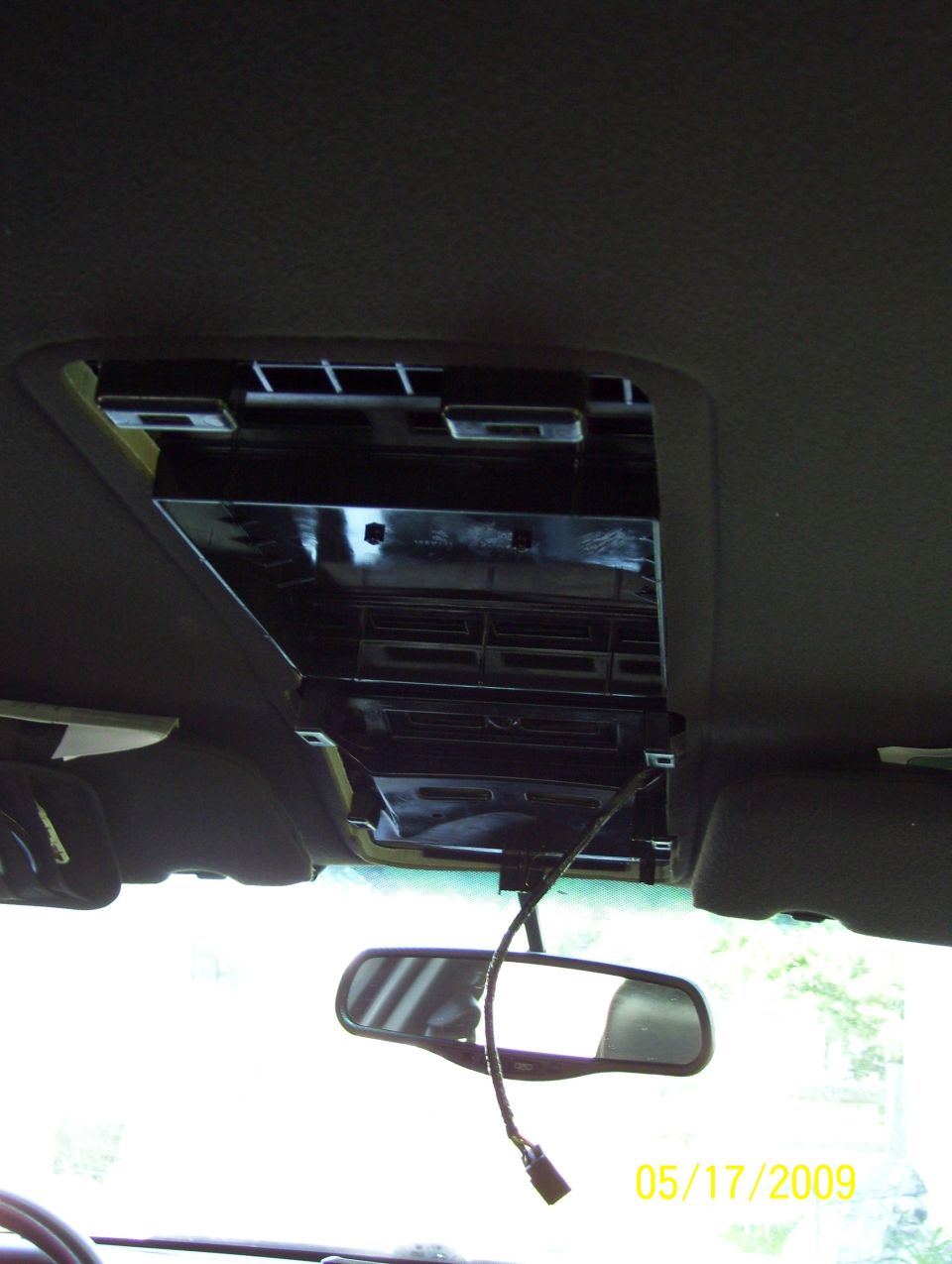 Interior shot of a car's ceiling with the overhead console removed, showing wiring and the rearview mirror