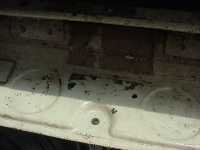 Close-up of white sheet metal panel with round stampings, rust spots, and chipped paint on a 1962 Ford F-100