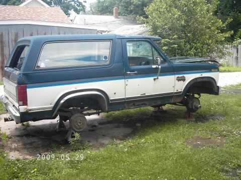 1986 Ford Bronco - This two-tone Ford Bronco is missing its wheels and is elevated on jack stands in a grassy yard.