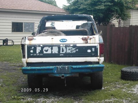 1986 Ford Bronco - Rear view of a weathered white Ford Bronco with a blue bumper and visible rust.