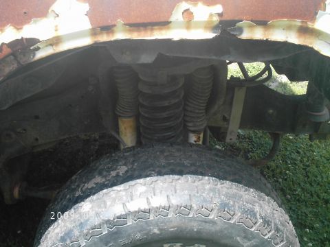 1986 Ford Bronco - Close-up view of the front suspension and tire of a vehicle, showing significant rust and wear.