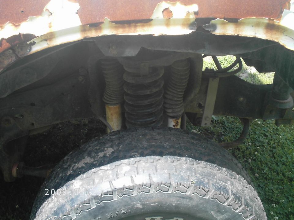 Rusty front wheel well with exposed suspension components and a worn tire