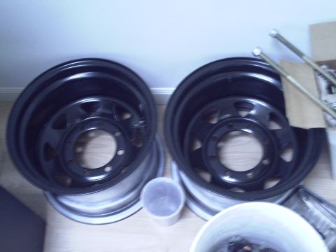 1990 Ford Bronco - Two black steel wheels are shown, possibly for a truck or SUV, with mounting hardware nearby.