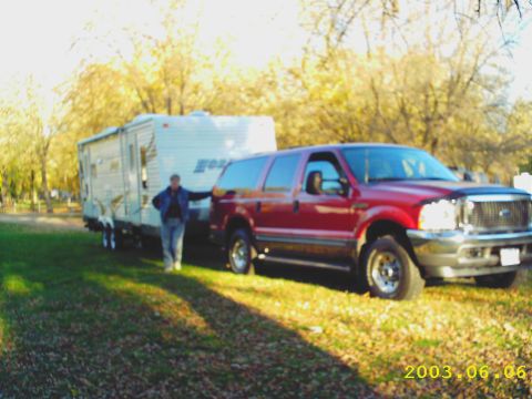 2003 Ford Excursion - A person stands next to a red Ford Excursion that is hitched to a travel trailer.