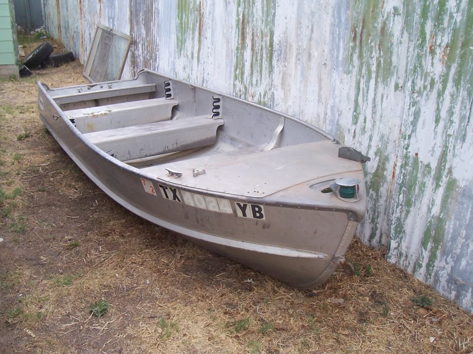 Aluminum boat with TX YB license plate, leaning against a corrugated metal wall