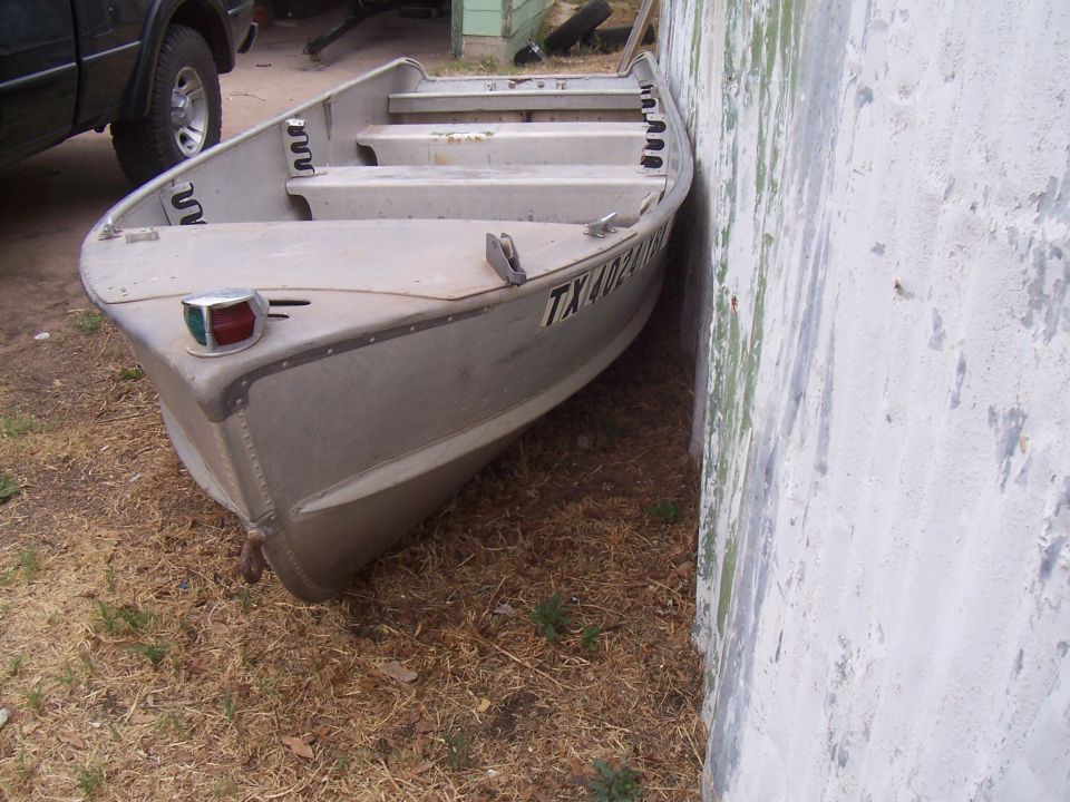 aluminum fishing boat parked next to a wall, TX license plate visible