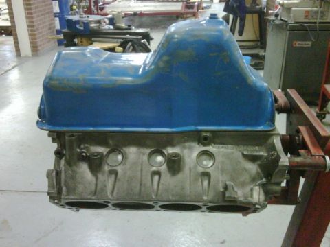 1996 Ford Bronco - An engine block with a blue oil pan is mounted on a red stand in a workshop.