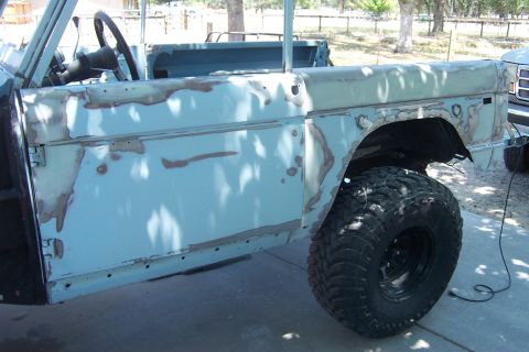 1976 Ford Bronco - This light blue SUV body shows primer patches and a large off-road tire, indicating it is undergoing bodywork.