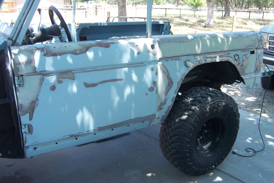 Side view of light blue SUV body with primer patches and large off-road tire