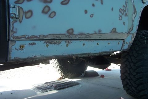 1976 Ford Bronco - Vehicle body panel showing rust damage and primer, likely undergoing repair.