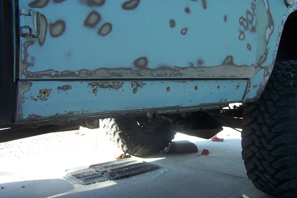 Close-up of a rusted blue vehicle side panel with primer showing through