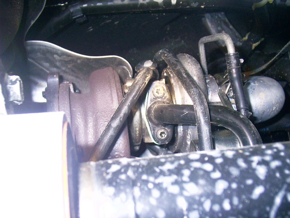 Dirty engine bay close-up with black vacuum hoses and Torx-screwed metal bracket