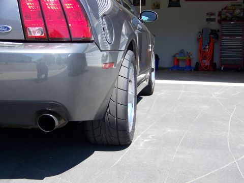 1993 Ford Bronco - The rear view of a Ford Mustang, highlighting its wide tire and exhaust pipe, parked in a garage setting.