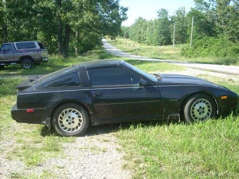 1989 Nissan 300ZX - Side view of a black 1989 Nissan 300ZX parked on grass with a dirt road and trees in the background.
