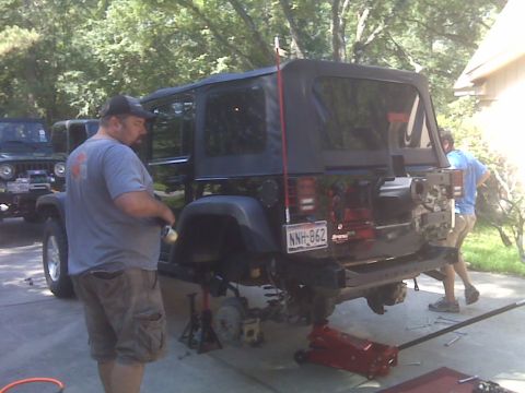 2008 Jeep Wrangler - A black 2008 Jeep Wrangler is shown with its rear suspension being worked on, with another Jeep visible in the background.