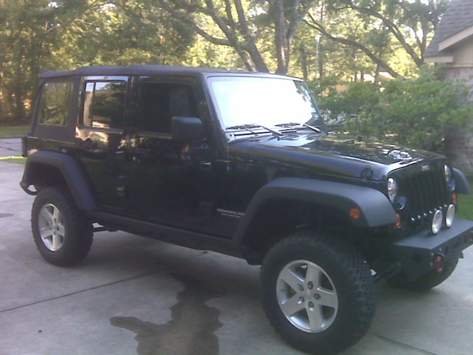 Black Jeep Wrangler with aftermarket bumper and lights, viewed from the front-right