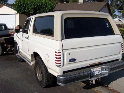 1991 Ford Bronco - This white Ford Bronco has a tan removable top and shows signs of rust around the tailgate.
