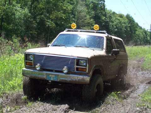 1986 Ford Bronco - Muddy 1986 Ford Bronco off-roading with smiley face lights on the roof rack.