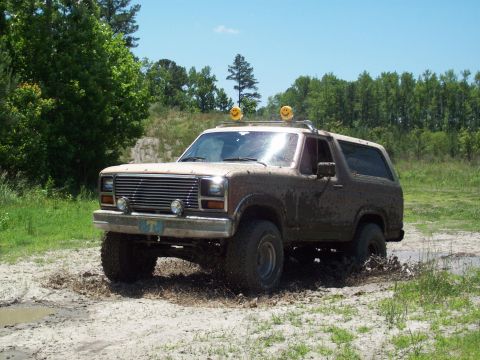 1986 Ford Bronco - This Ford Bronco is navigating a challenging muddy terrain, equipped with unique smiley face lights.