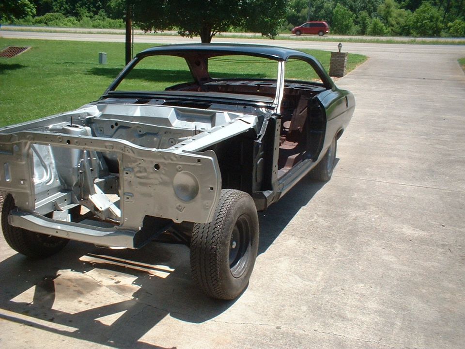 Stripped 1960s hardtop coupe body shell in primer and black paint on a driveway