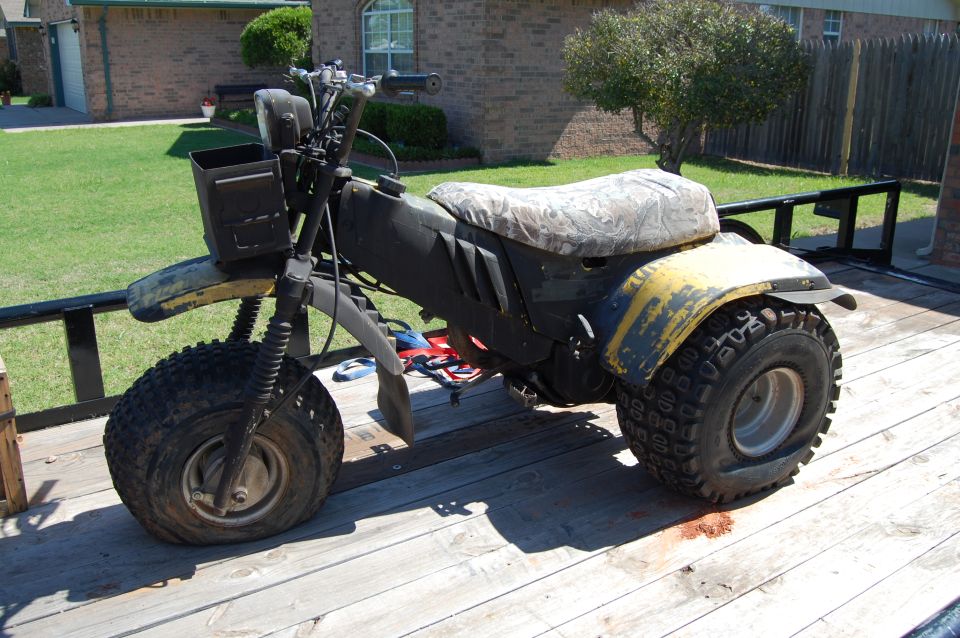 Yellow three-wheeled ATV with camouflage seat on a wooden trailer