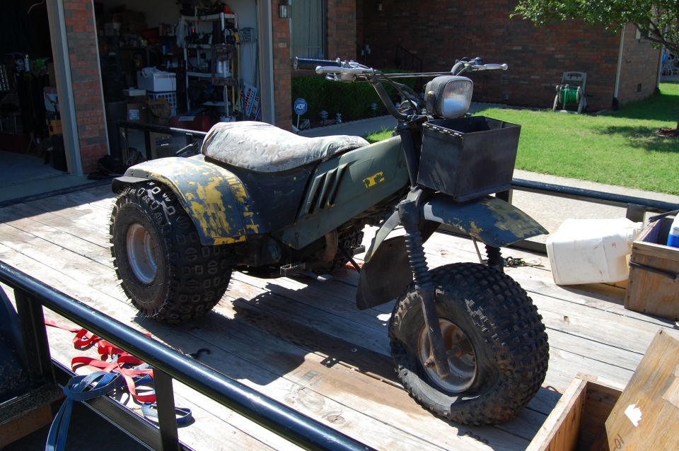Green and yellow three-wheeled ATV with a flat front tire, on a trailer