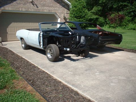 1970 Ford Torino - Two classic cars are parked on a driveway in front of a garage, both in various stages of restoration.