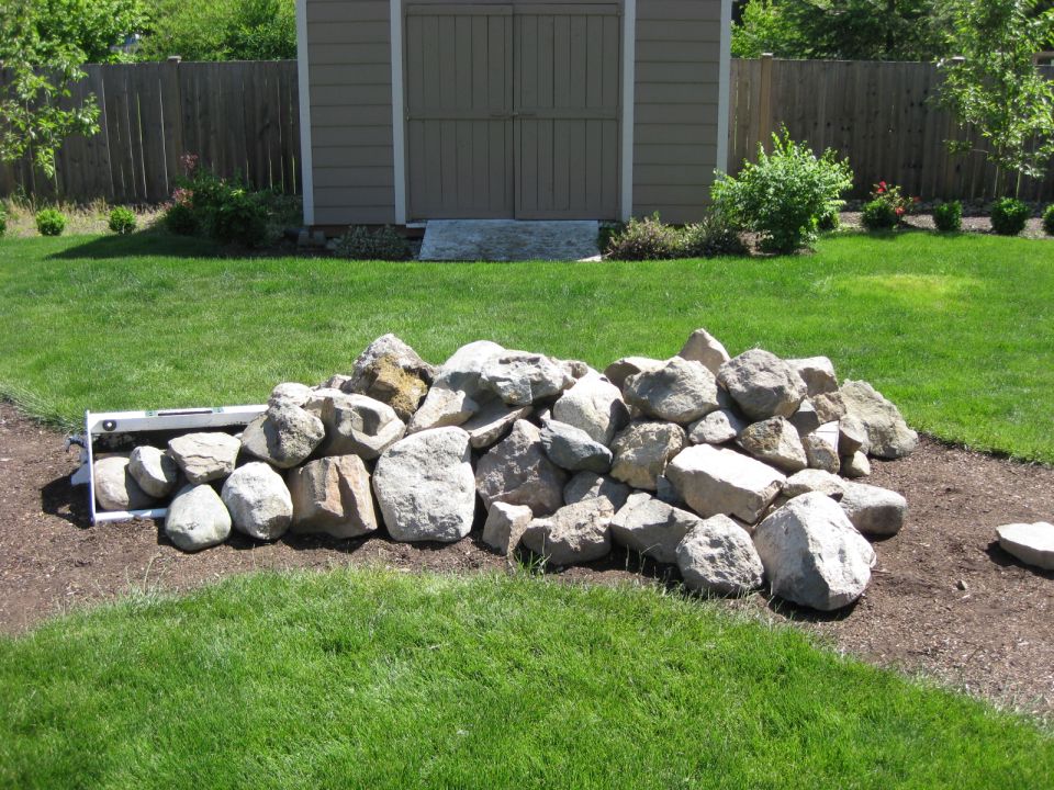 Pile of rocks in front of a shed and fence