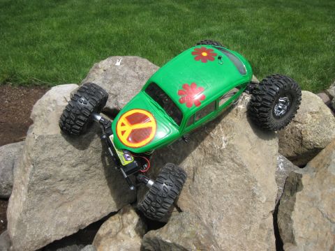 2010 Ford Pickup - A green remote control rock crawler toy car with peace sign and flower decals is positioned on large rocks.