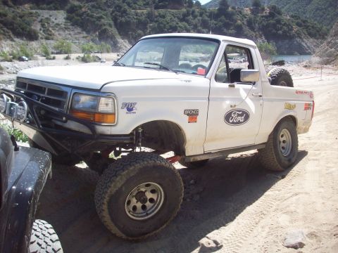 1995 Ford Bronco - Modified 1995 Ford Bronco seen off-roading in a natural landscape with another vehicle partially visible.