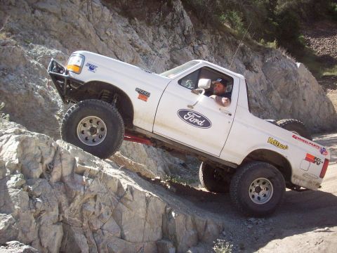 1995 Ford Bronco - A white 1995 Ford Bronco navigates a steep, rocky trail, its off-road capabilities.
