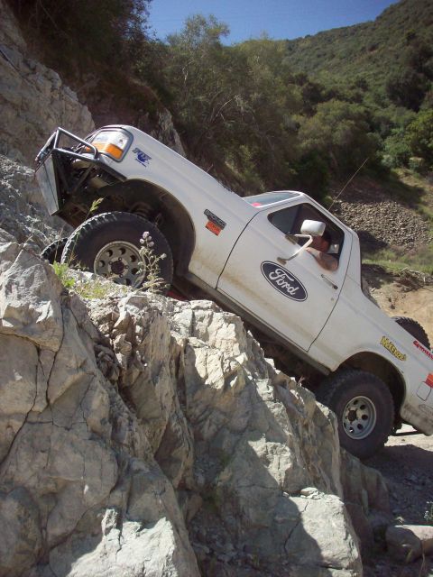 1995 Ford Bronco - A white Ford Bronco navigates a steep, rocky trail with a modified front bumper.