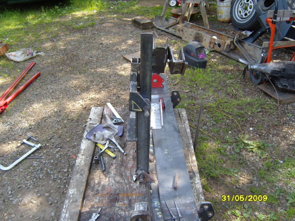 Metal fabrication equipment on a wooden workbench outdoors, with tools scattered around