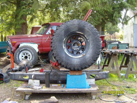 1989 Ford Bronco - A red pickup truck is partially visible behind a large spare tire and bumper assembly.