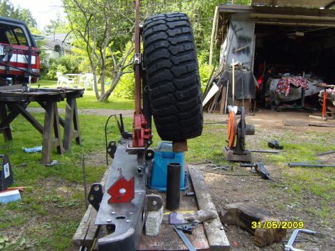 1989 Ford Bronco - A spare tire is mounted on a jack, part of a metal frame assembly, with a workshop in the background.