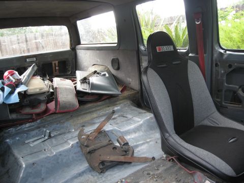 1986 Ford Bronco - The interior of a vehicle is shown with a racing seat and various parts scattered around the floor.