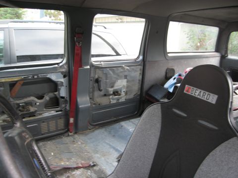1986 Ford Bronco - The interior of a vehicle shows racing seats and exposed door panels, with another vehicle visible outside.