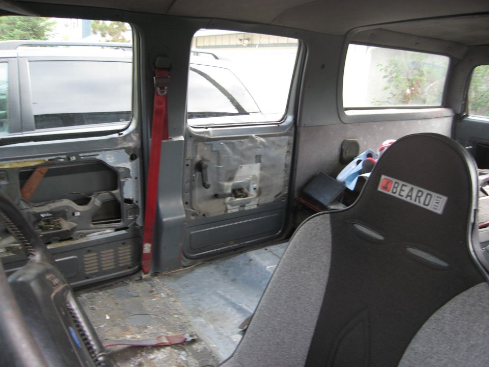 Interior of a vehicle with racing seats and exposed door panels. A second vehicle is visible through the windows