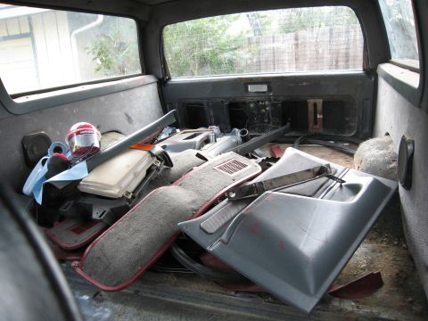1986 Ford Bronco - Various interior parts, including door panels and carpet, are stored within the cargo area of a vehicle.