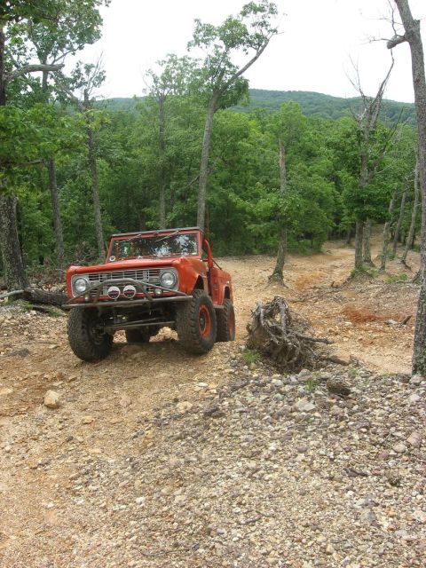 1987 Suzuki Samurai - An orange off-road vehicle navigates a rocky trail surrounded by trees.
