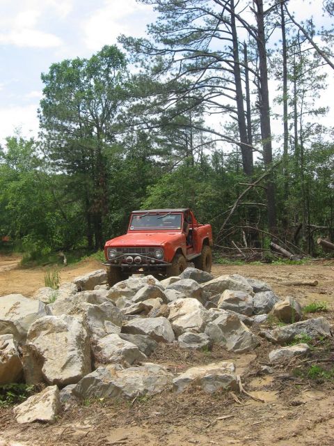 1987 Suzuki Samurai - An orange off-road vehicle navigates a rocky terrain in a wooded area.