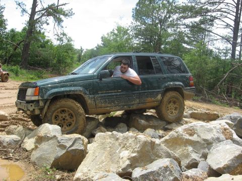 1987 Suzuki Samurai - Jeep Grand Cherokee tackling a rocky off-road course with a driver looking out the window.